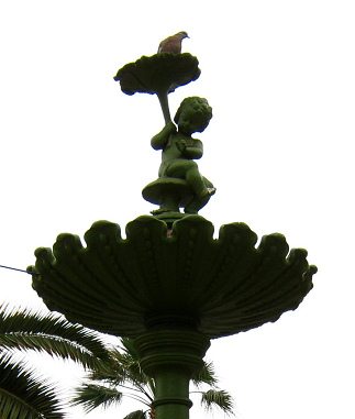 Kolumbusplatz, die kleine Kinderstatue auf
                        dem Brunnen, und da ist eine Taube oben drauf,
                        Nahaufnahme