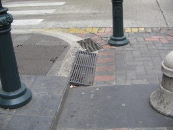Zentrum von Guayaquil, Trottoirauffahrt
                          in Metallgitter und Dolendeckel der
                          Kanalisation in engem Gitter