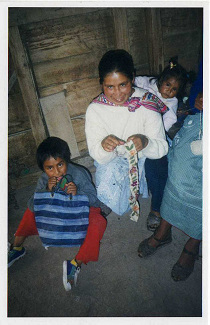 Bordadora con peque�o ni�o en la espalda y un otro
                ni�o en el piso