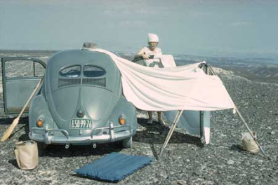 Maria Reiche in den 1950er Jahren mit einem
                        Volkswagen (VW Kfer) und einem Besen, um die
                        Linien zu putzen