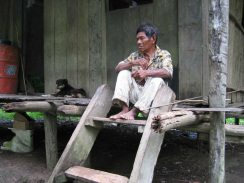 Amazonas-Flussdorf 02, ein Indigena-Mann
                          sitzt auf dem Vorplatz seines Pfahlhauses