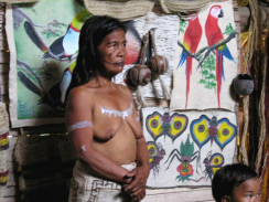 Amazonas-Flussdorf 03 bei Iquitos,
                          Indigena-Fraue vor einem Wandbehang mit roten
                          Papageien